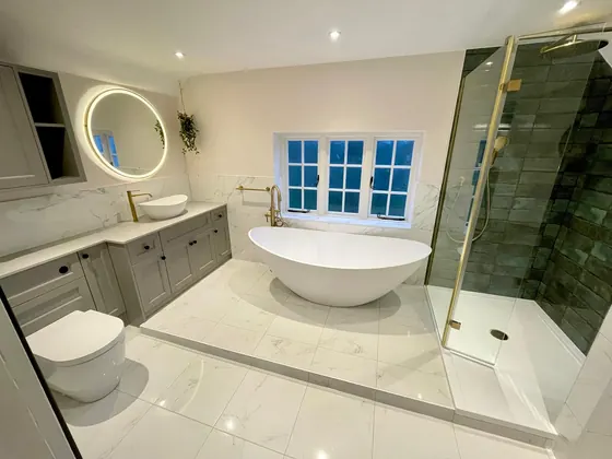 Bathroom with a freestanding bath, brass taps, marble effect tiling and a round backlit mirror