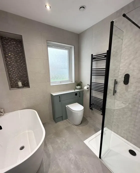 Bathroom with a freestanding bath, mosaic tiled niche, black towel rail and a sage green vanity unit